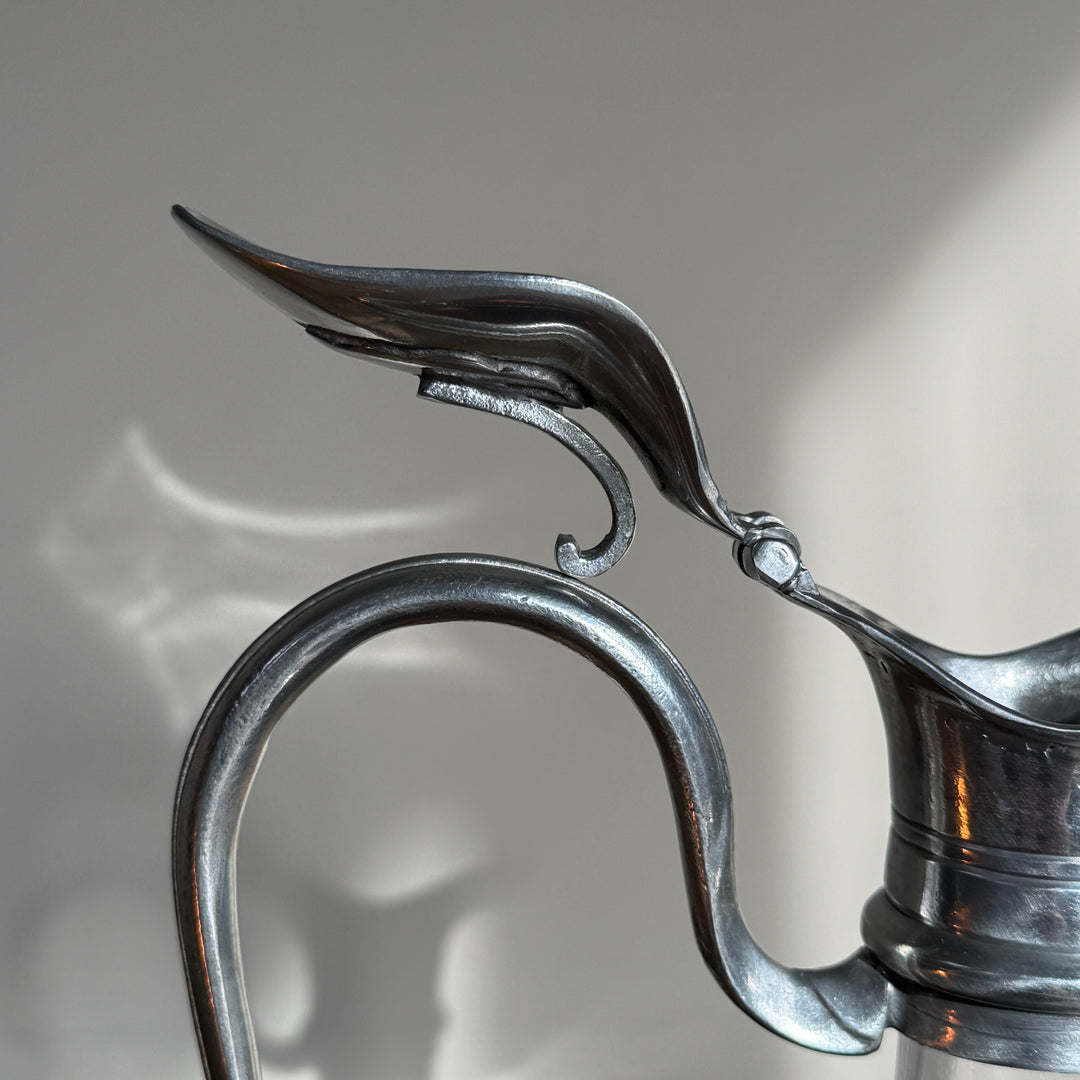 Detailed view of the curved pewter handle and decorative pouring spout on a French glass wine decanter, highlighting its traditional metalwork.