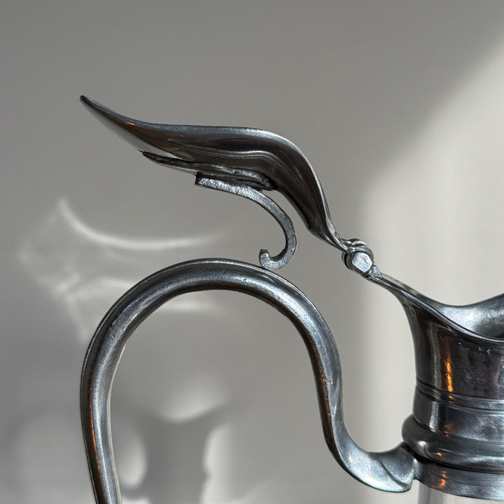 Detailed view of the curved pewter handle and decorative pouring spout on a French glass wine decanter, highlighting its traditional metalwork.