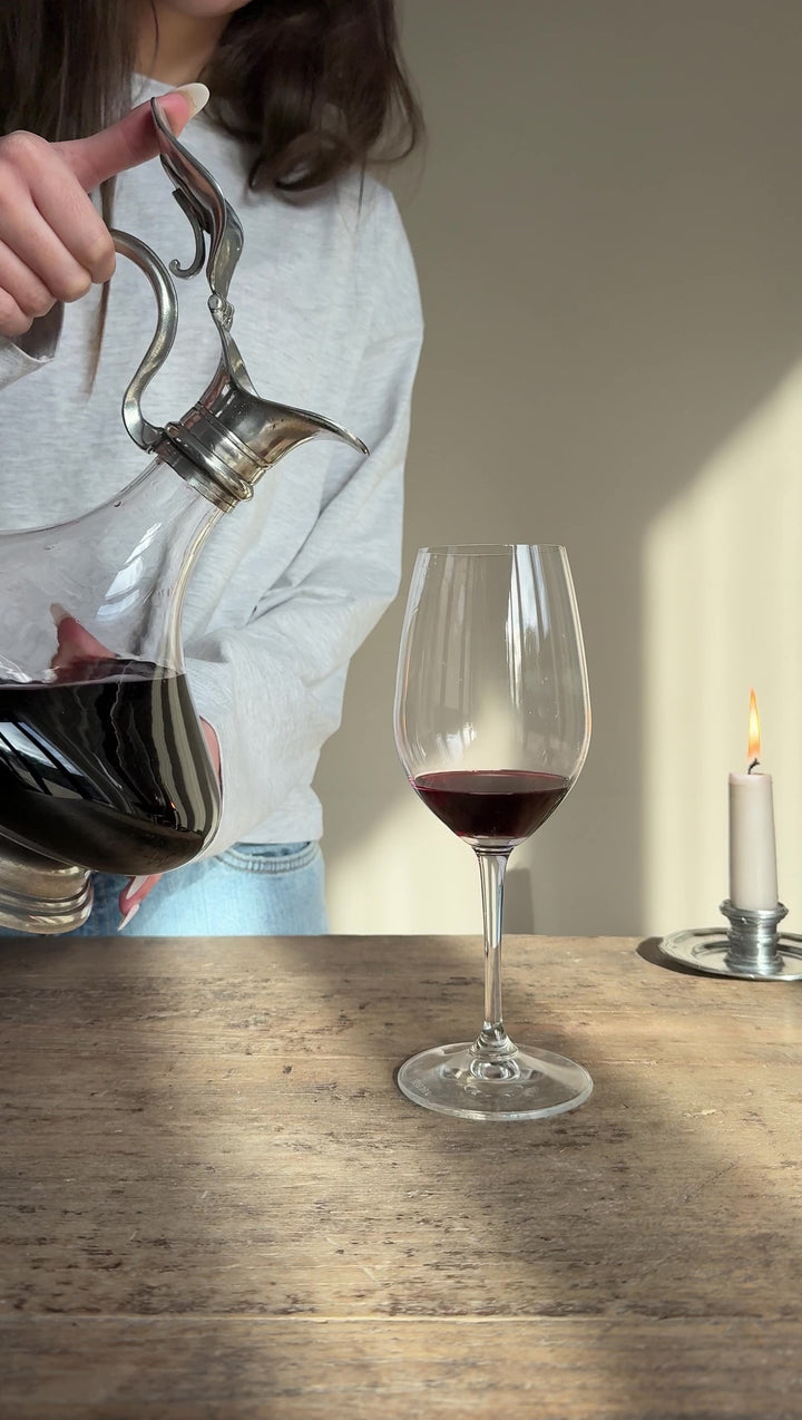 Video demonstrating red wine being poured from a French pewter and glass wine decanter with an ornate metal spout and handle.