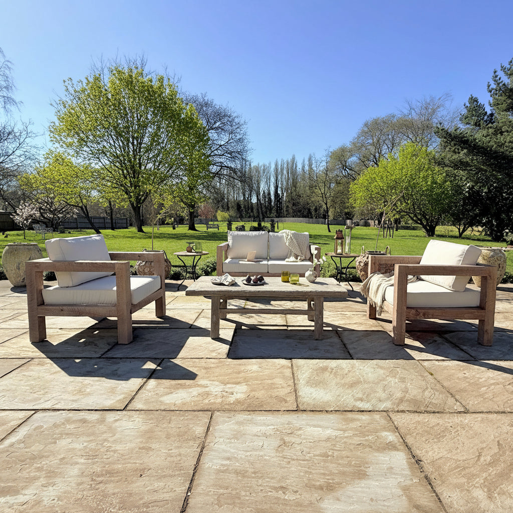 Outdoor patio set with chairs, table, and cushions on a stone patio with trees and grass in the background.