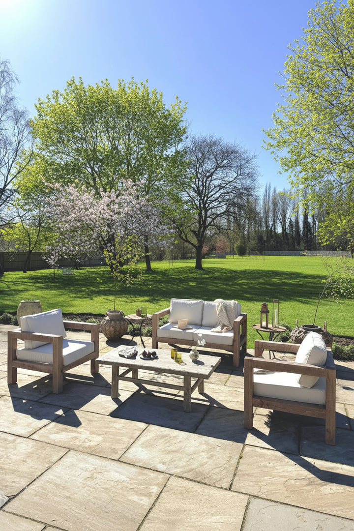 Outdoor patio set with wooden furniture and white cushions in a garden setting.